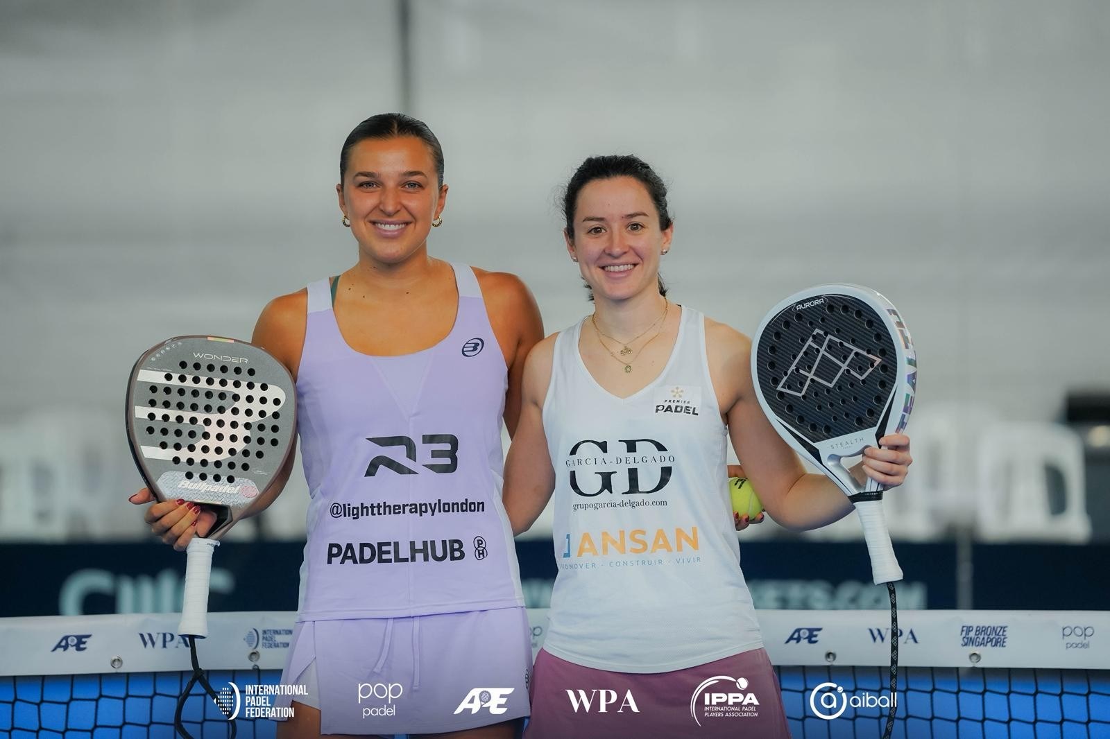 British padel player Catherine Rose smiling and holding a padel racket next to Spain's Lucia Perez Parra