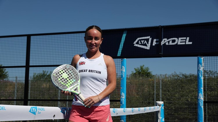British padel player Aimee Gibson holding her padel racket while stood on a padel court with the sign 'LTA Padel' behind her