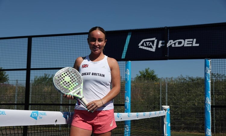 British padel player Aimee Gibson holding her padel racket while stood on a padel court with the sign 'LTA Padel' behind her