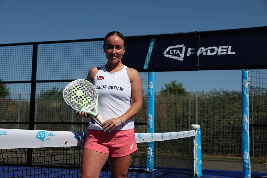 British padel player Aimee Gibson holding her padel racket while stood on a padel court with the sign 'LTA Padel' behind her