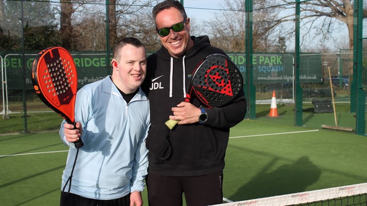 A young man with Downs Syndrome poses with a padel coach on an outdoor padel court