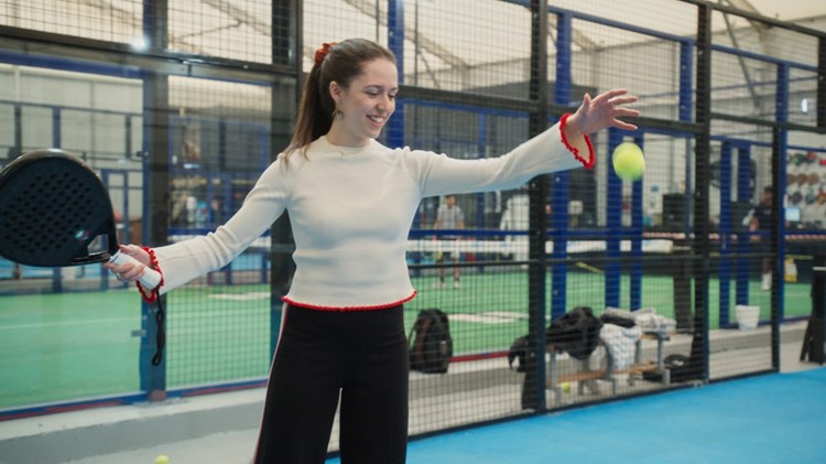 An image of a woman preparing to drop a padel ball and hit it with her racket on a padel court