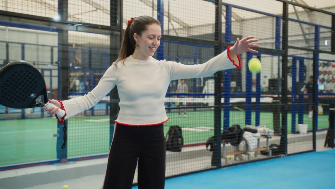 An image of a woman preparing to drop a padel ball and hit it with her racket on a padel court