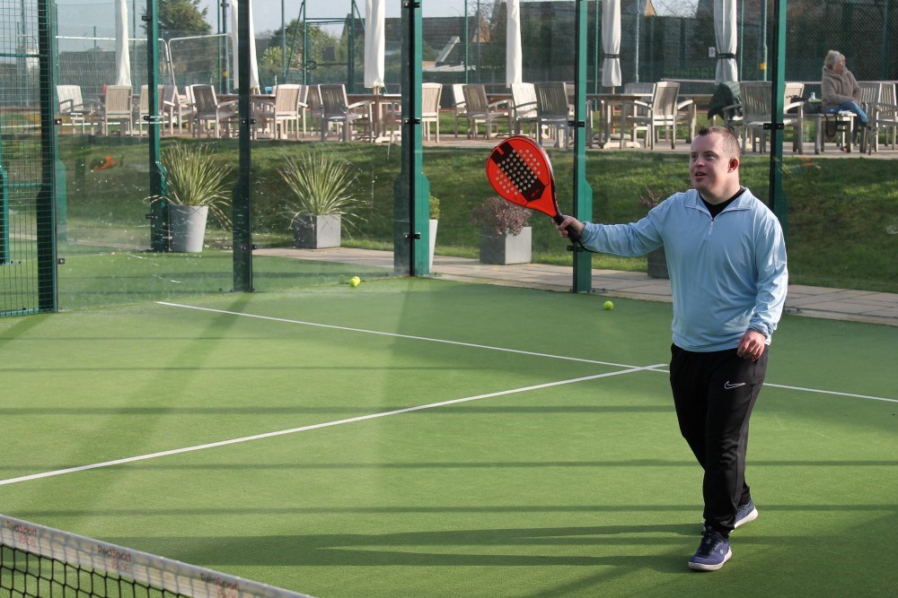 A young man with Downs Syndrome hits a padel shot on an outdoor court