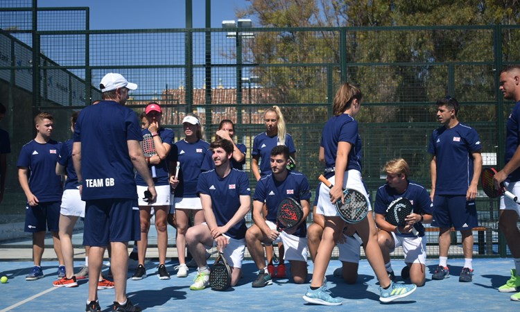A group of padel players all knealt down on a padel court holding their rackets