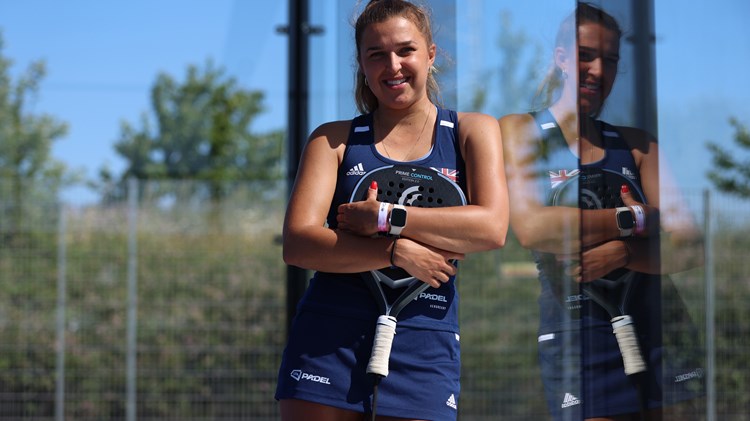 Catherine Rose leaning against the padel court glass with her racket