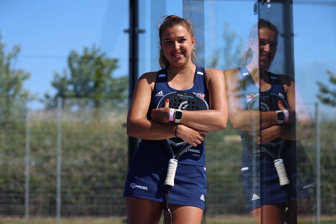 Catherine Rose leaning against the padel court glass with her racket