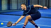 Louie Harris bending down to retrieve a ball with his padel bat on court