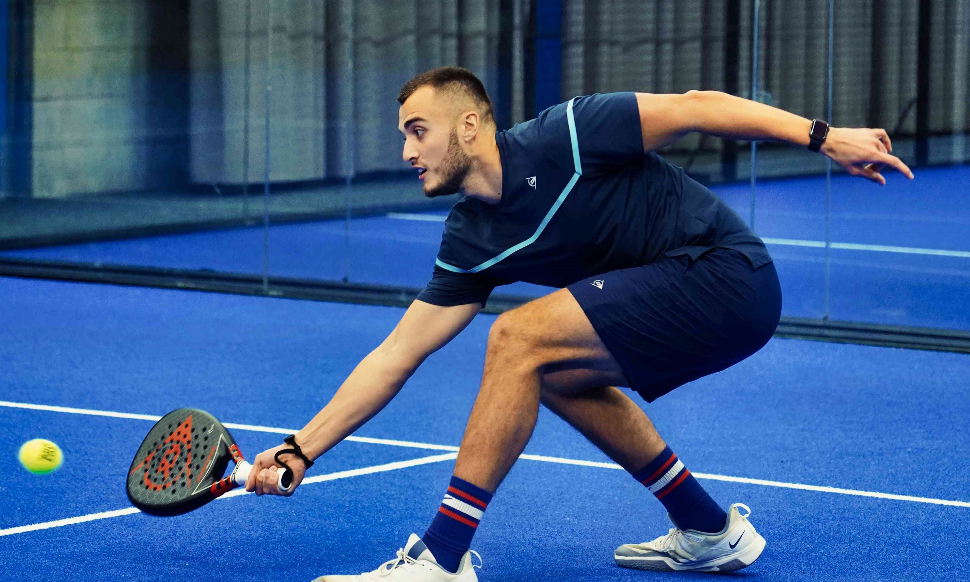 Louie Harris bending down to retrieve a ball with his padel bat on court