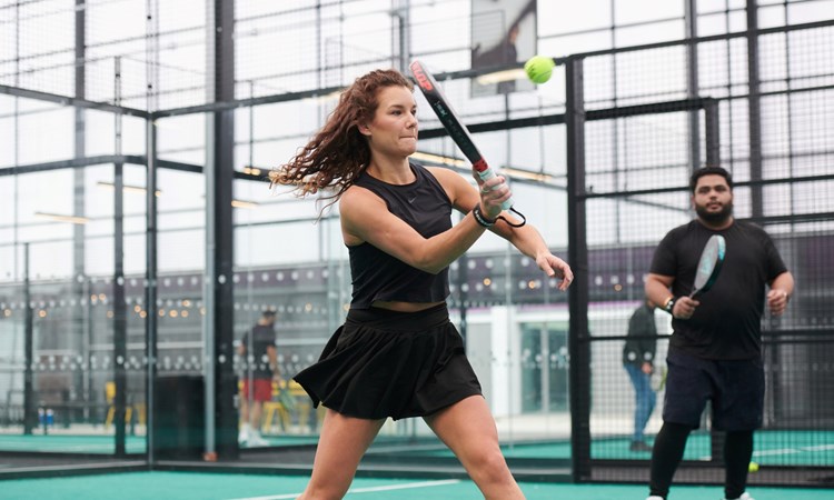 two people stood on a padel court, with one woman preparing to hit a volley at the net during a competition