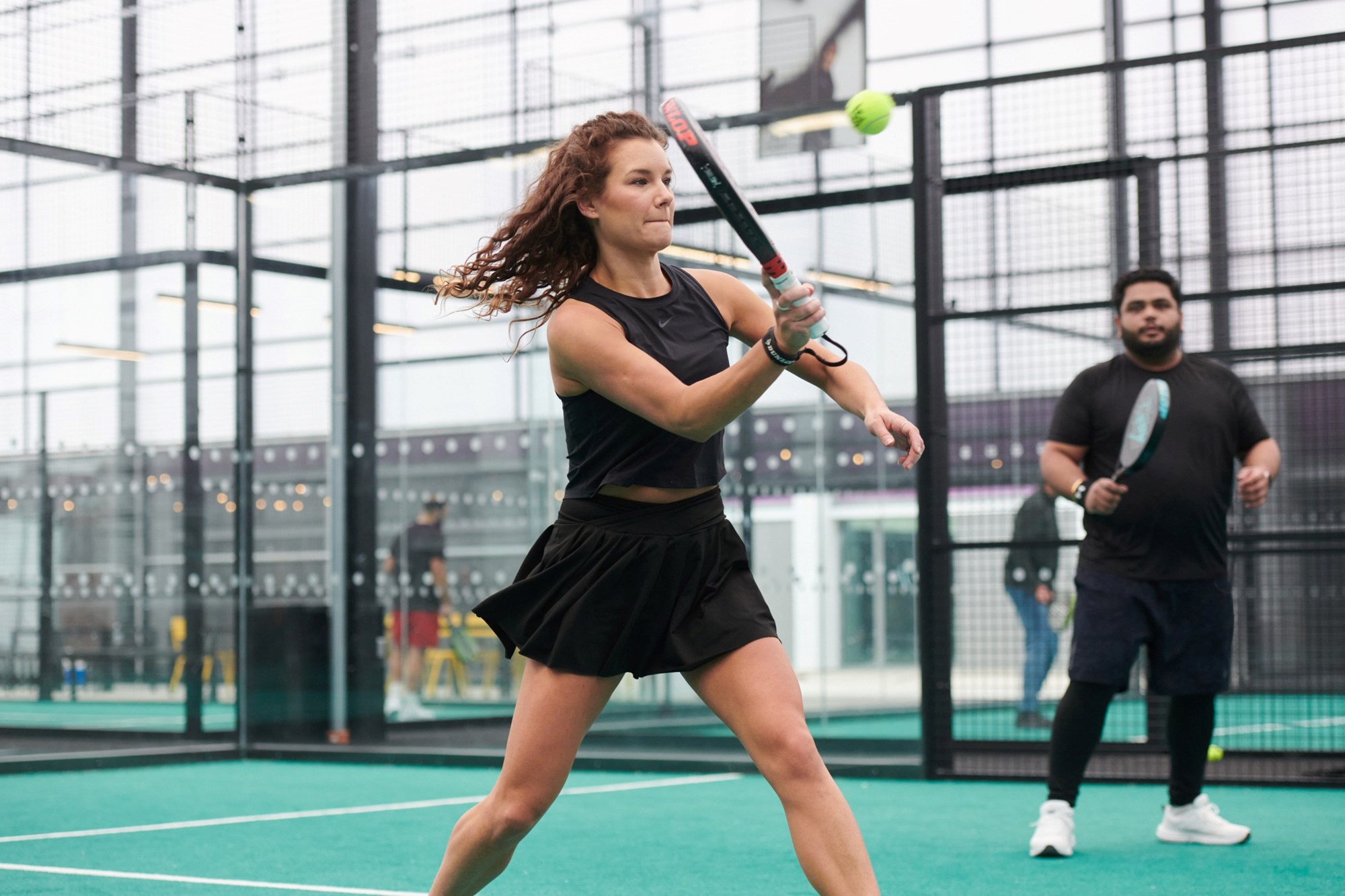 two people stood on a padel court, with one woman preparing to hit a volley at the net during a competition