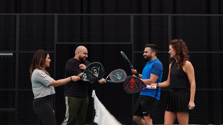 Four padel players tapping their rackets over the net