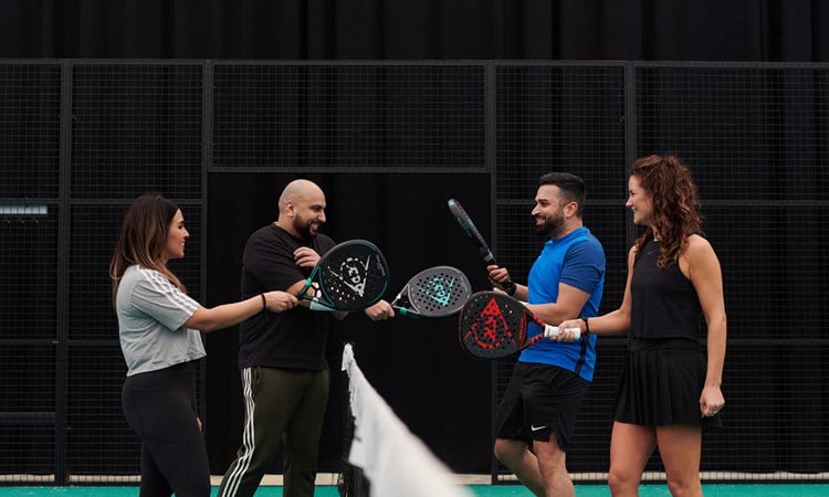 Four padel players tapping their rackets over the net