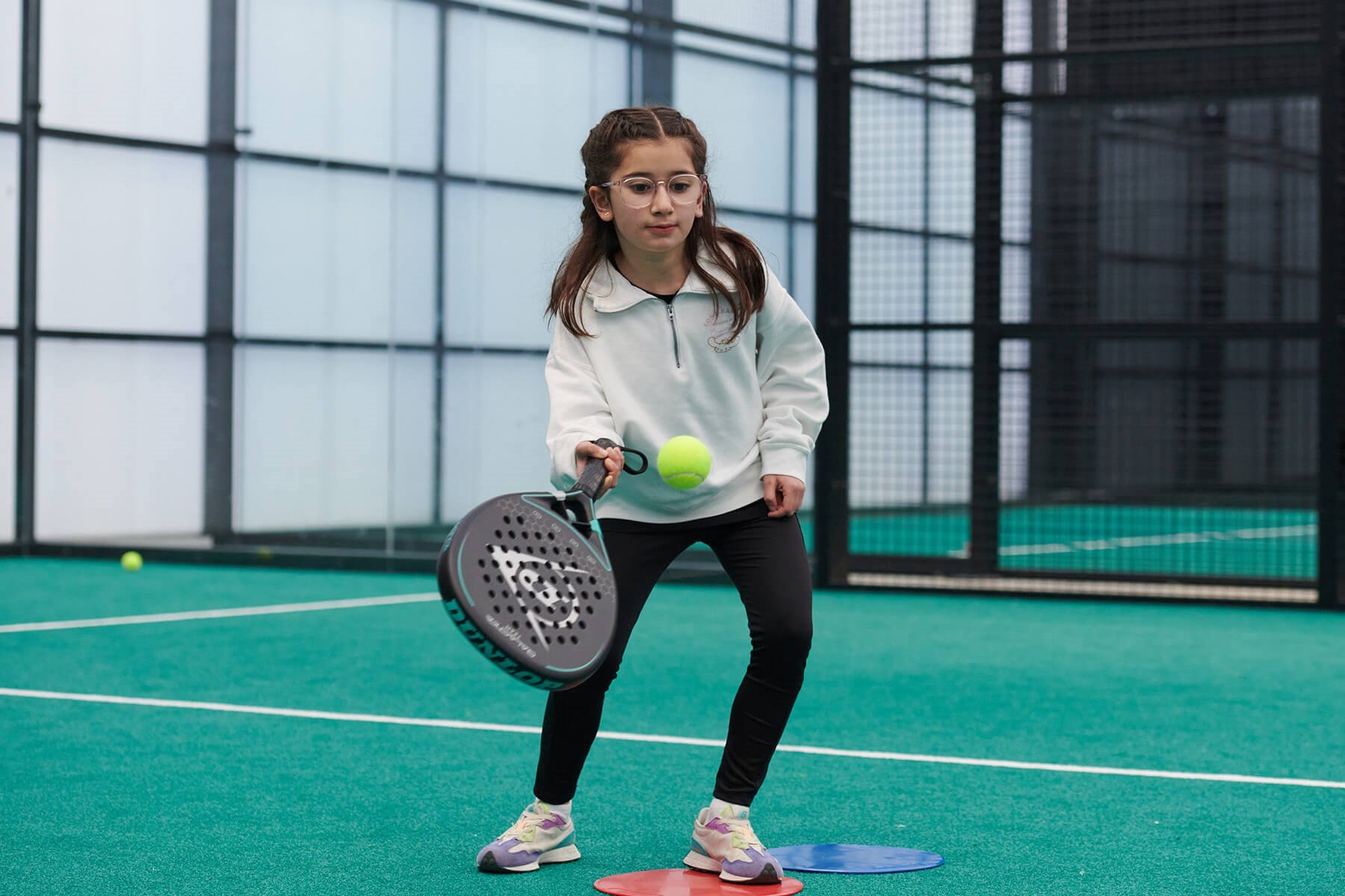 A young girl about to hit a padel ball with her racket