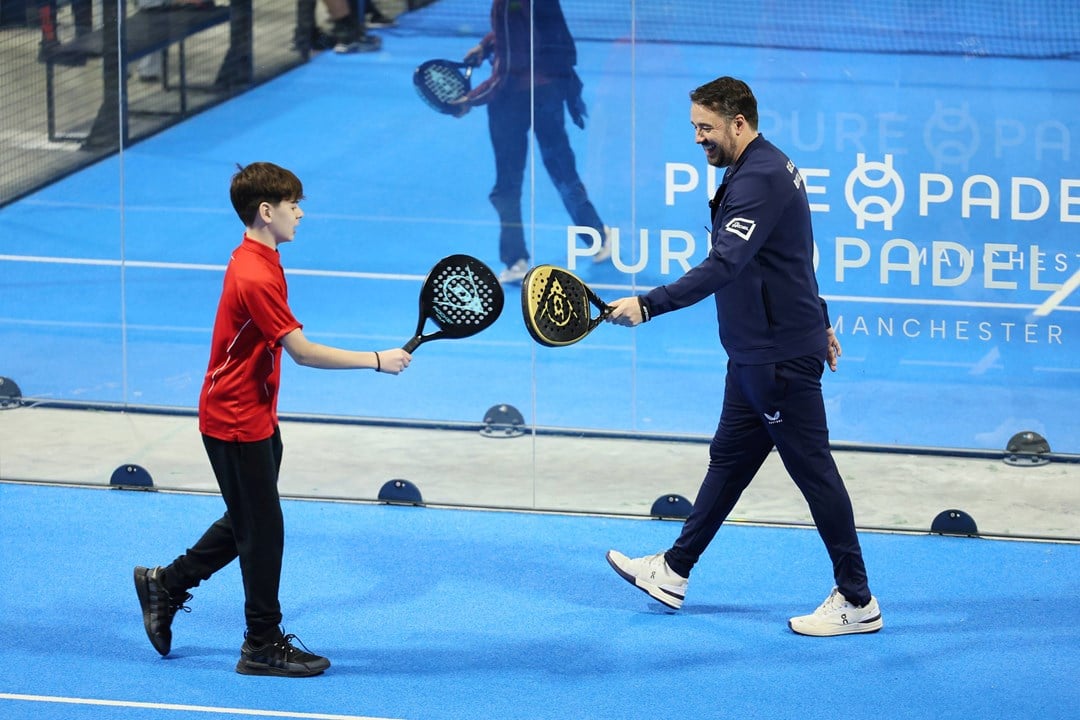 Jason Manford on the padel court with a junior player smiling and tapping rackets