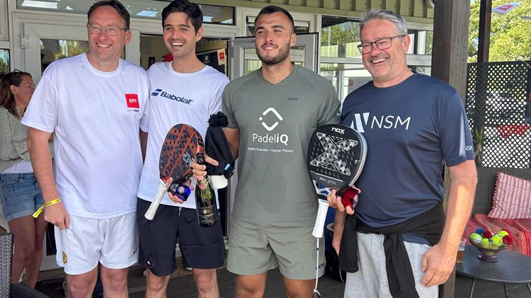 Louie Harris and Rafael Vega holding their padel bats, a bottle of champagne and their trophies alongside two men at the Padel British Tour event in Guernsey