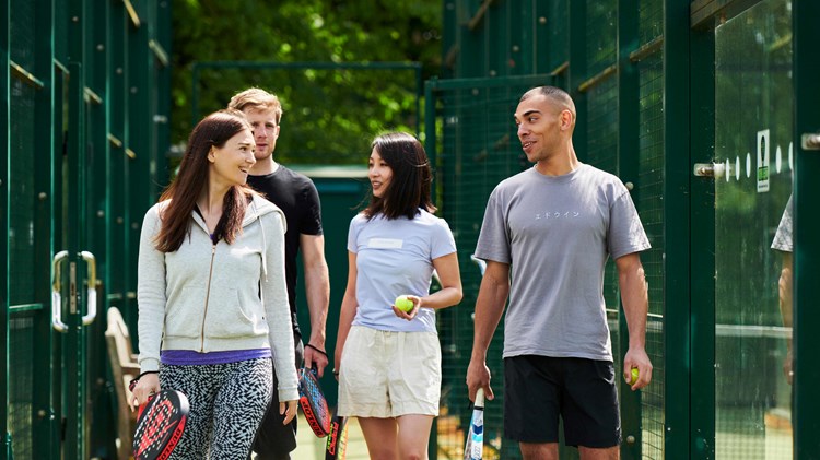 A group of four people walking to a padel court with their rackets in hand