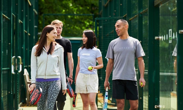 A group of four people walking to a padel court with their rackets in hand