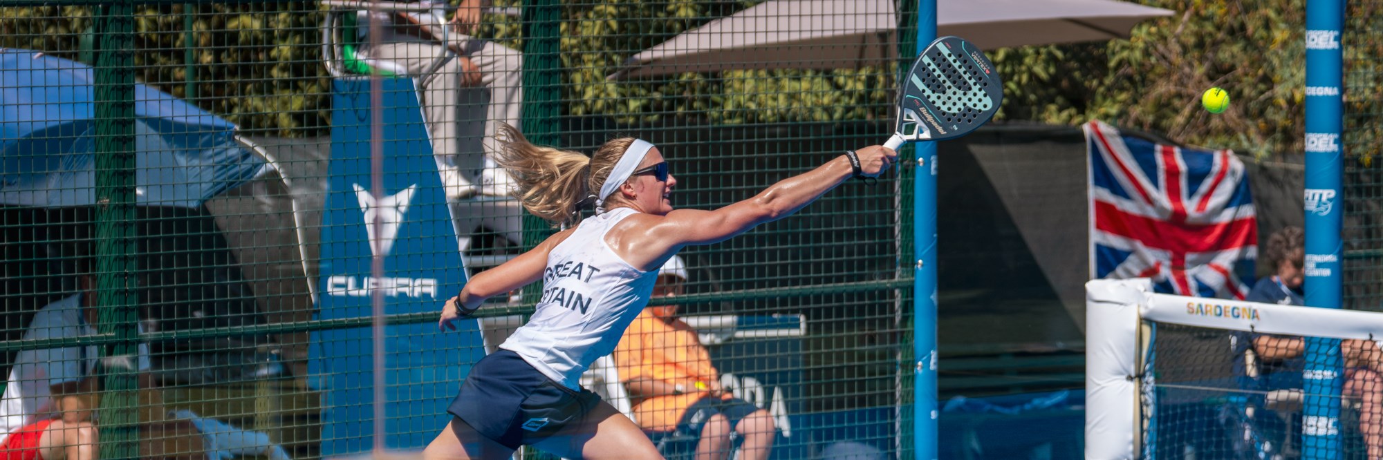 Victoria Nicholas running across the padel court with arm outstretched to reach the ball
