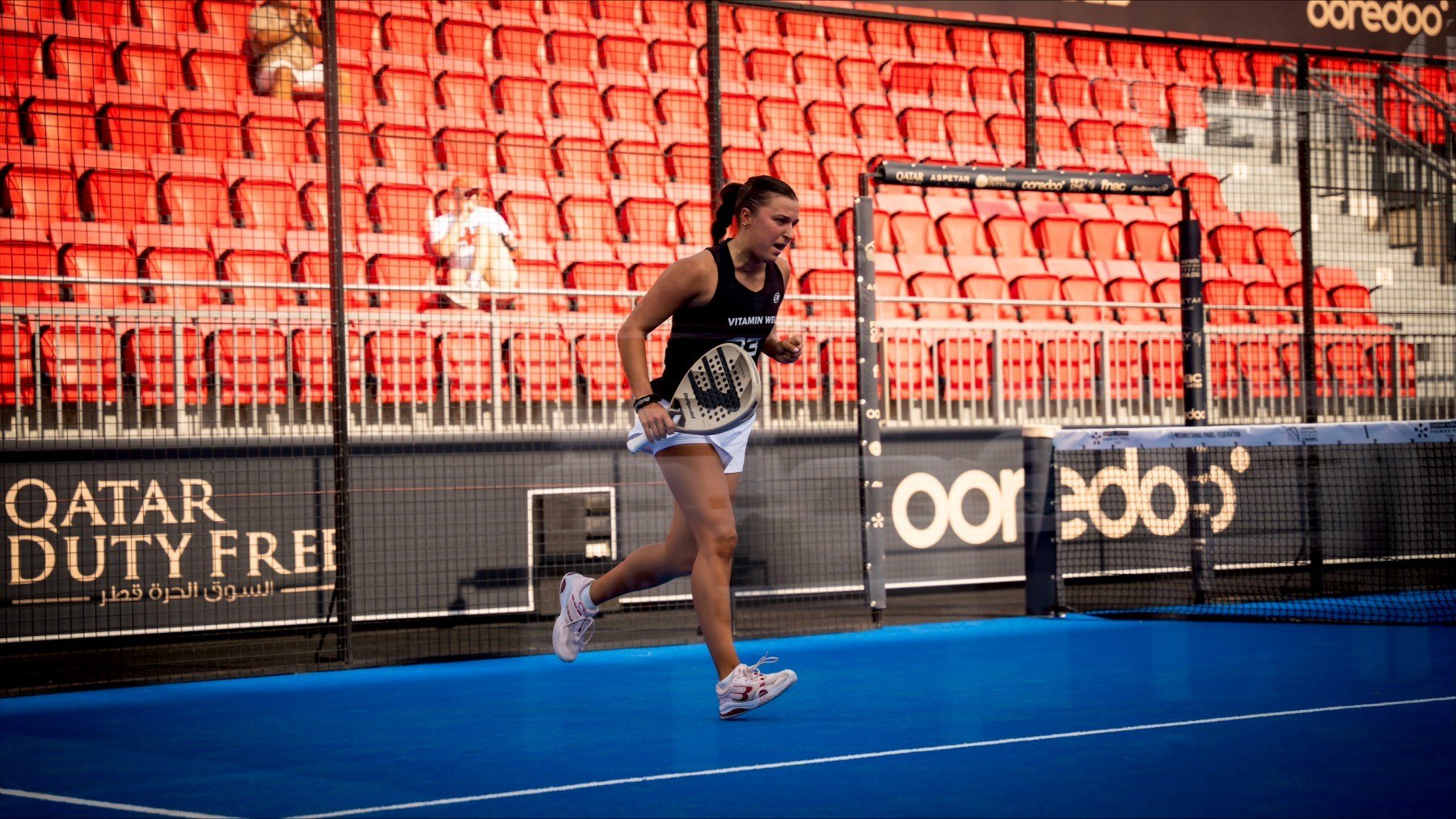 British padel player Catherine Rose running across a padel court while holding a padel racket in her hand and clenching her fist
