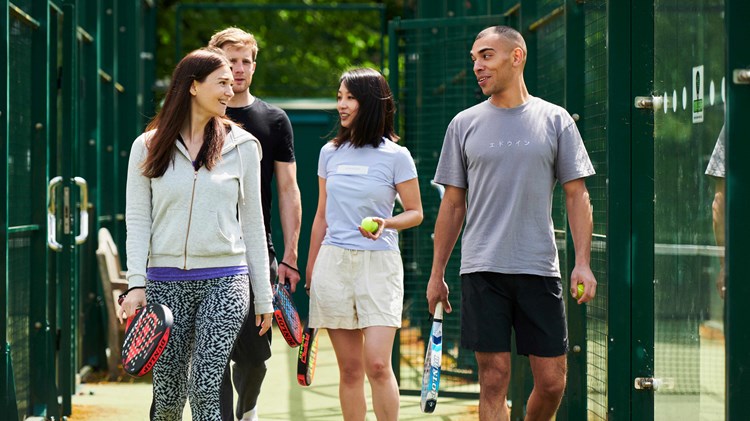 A group of four people walking to a padel court with their rackets in hand