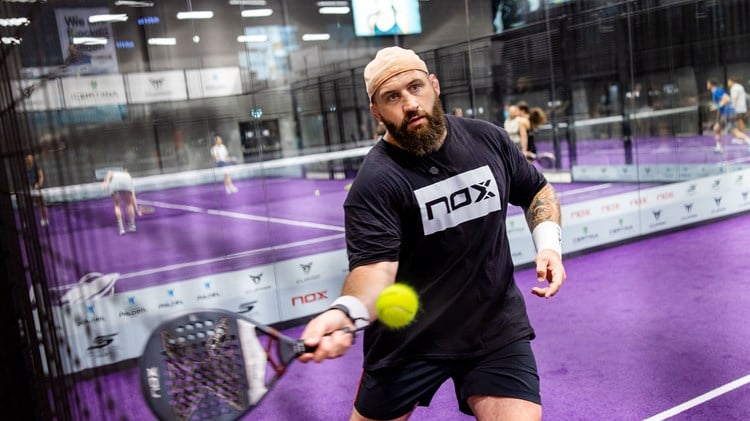 Former England rugby player Joe Marler holding a padel racket while preparing to hit a ball on a padel court