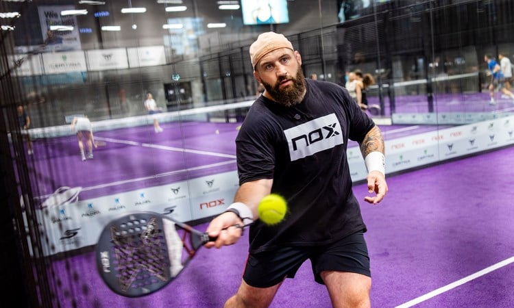 Former England rugby player Joe Marler holding a padel racket while preparing to hit a ball on a padel court