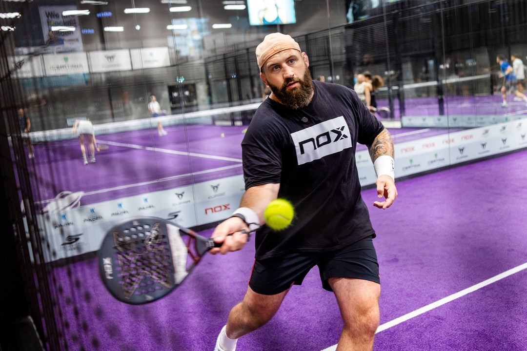 Former England rugby player Joe Marler holding a padel racket while preparing to hit a ball on a padel court