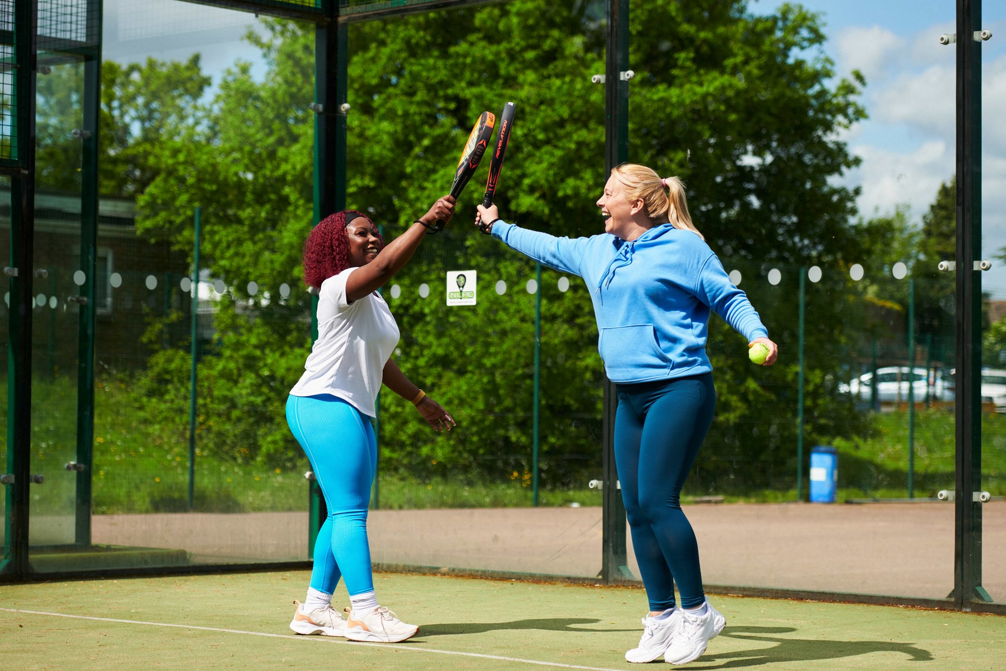 Two players smiling and tapping padel rackets