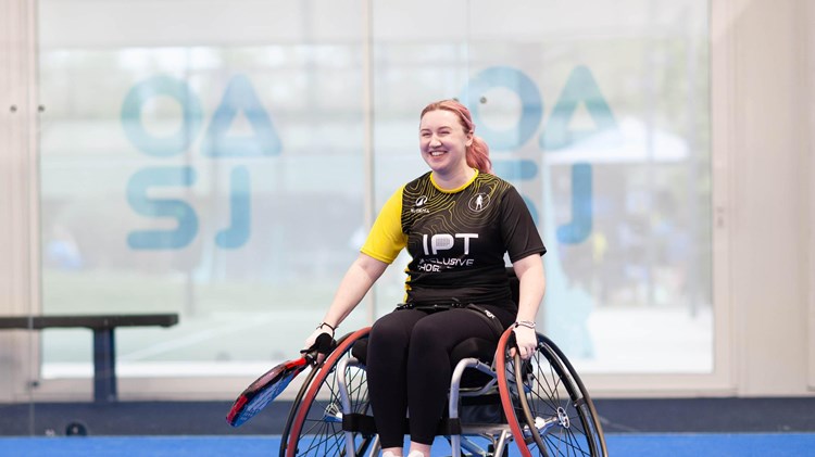 Wheelchair padel player Kristen Paskins smiling while sat in her wheelchair and holding a padel racket at the Inclusive Padel Tour