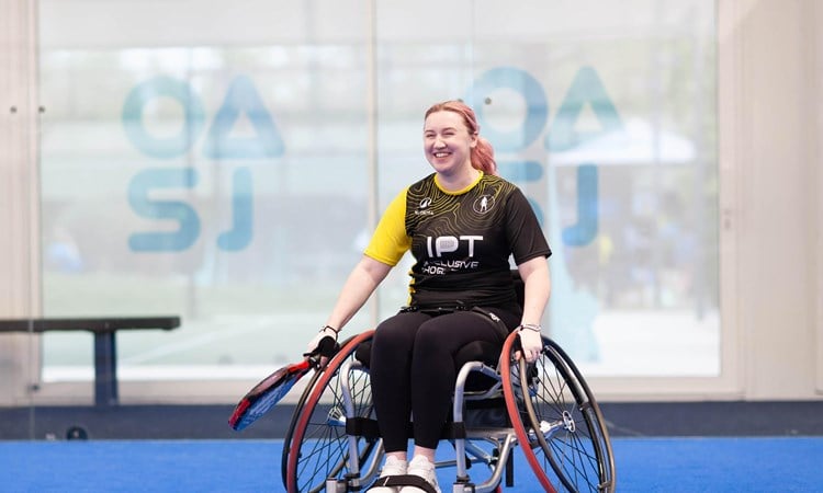 Wheelchair padel player Kristen Paskins smiling while sat in her wheelchair and holding a padel racket at the Inclusive Padel Tour
