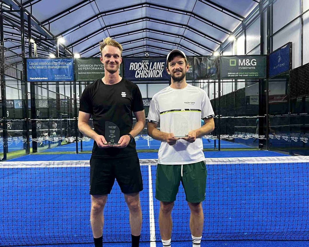 British padel players Nicholas Hatchett and Sam Macneil holding their trophies and smiling on court at the LTA Padel British Tour event at Rocks Lane, Chiswick