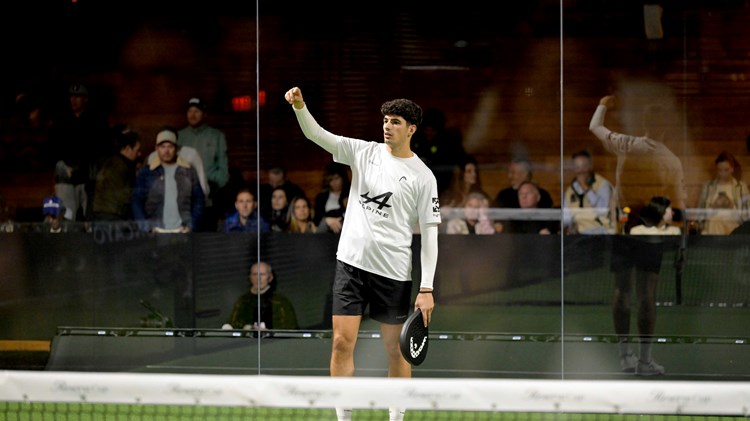 Spanish padel player Arturo Coello holding a padel racket and raising his arm up on a green padel court
