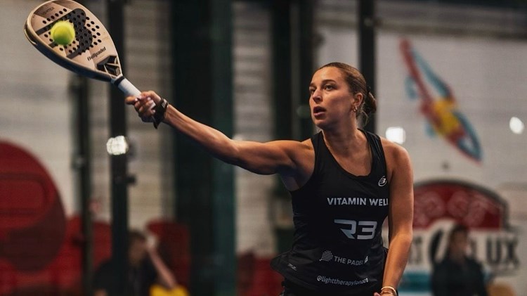 A woman wearing a bacl sports outfit hits a tennis ball with a padel racket