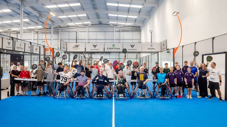 A group of players at a Pro-Am Padel Community Day on court raising their rackets as they pose for a photo