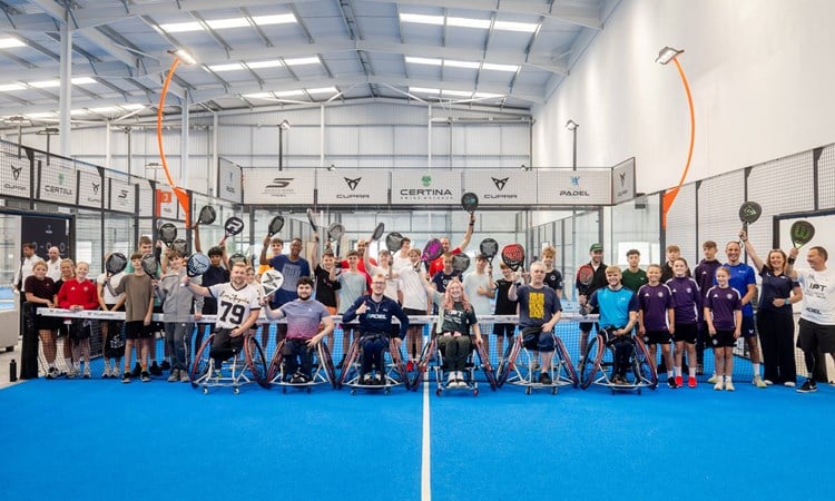 A group of players at a Pro-Am Padel Community Day on court raising their rackets as they pose for a photo