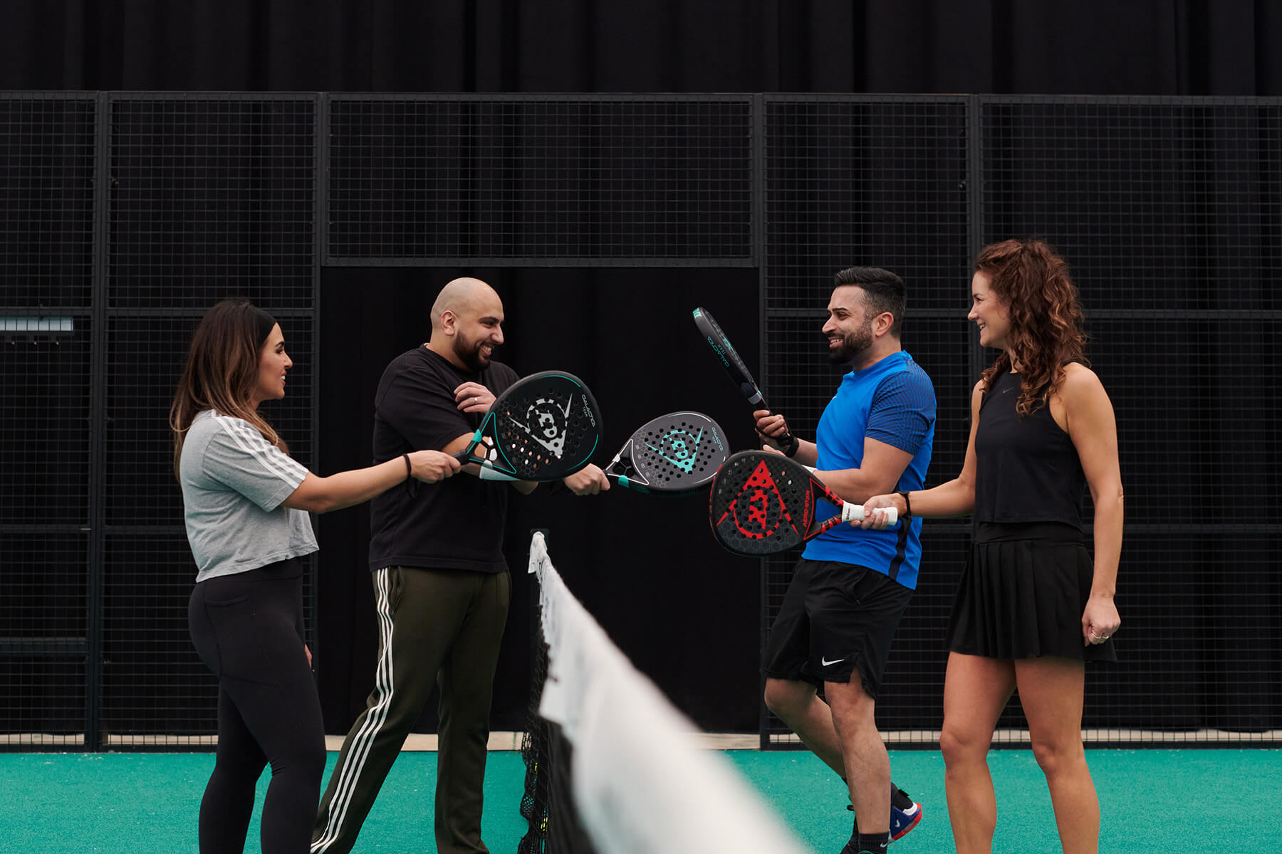 Four padel players tapping their rackets over the net
