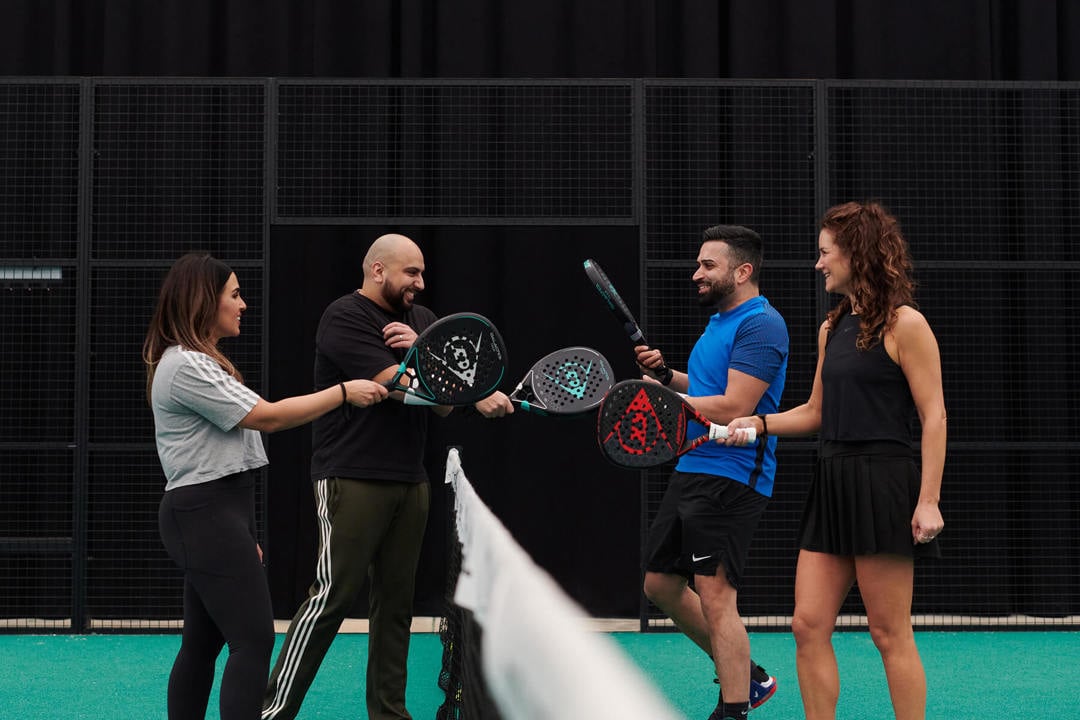 Four padel players tapping their rackets over the net
