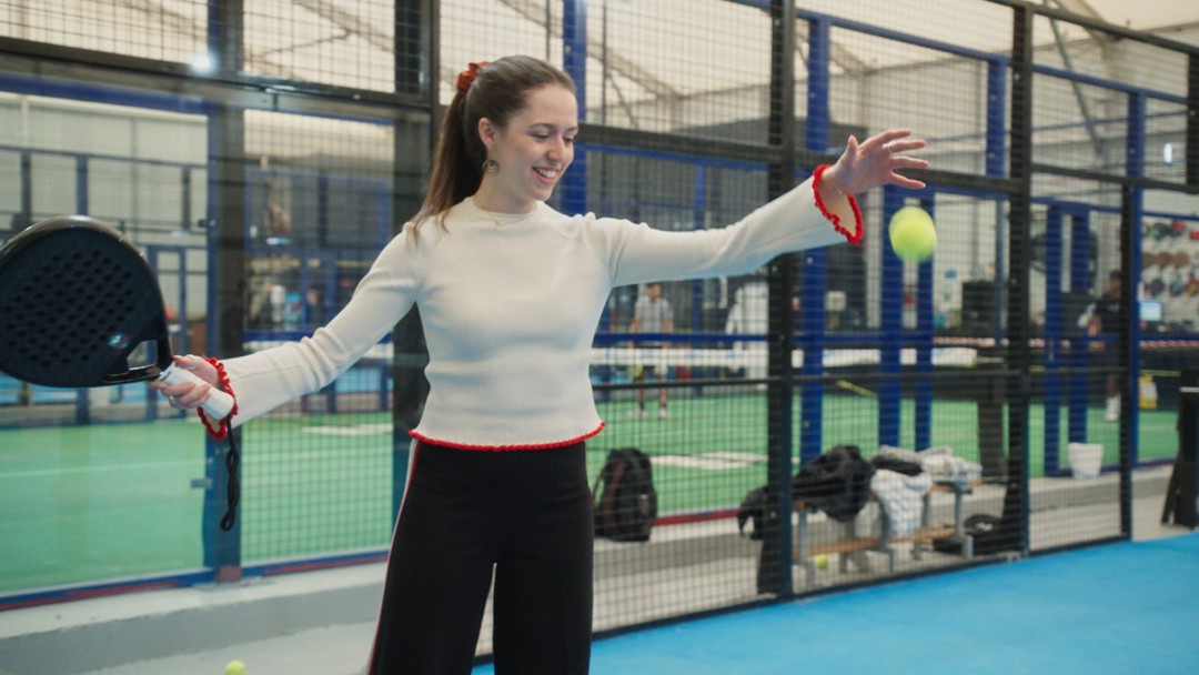 An image of a woman preparing to drop a padel ball and hit it with her racket on a padel court