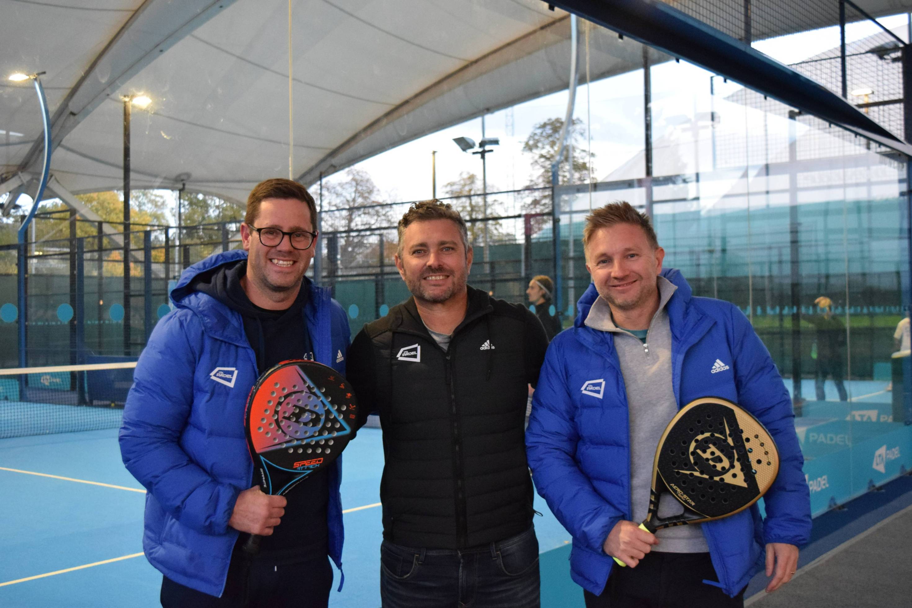 Matt Stanforth, Jordi Munoz and Tom Murray holding padel rackets and stood in front of padel courts