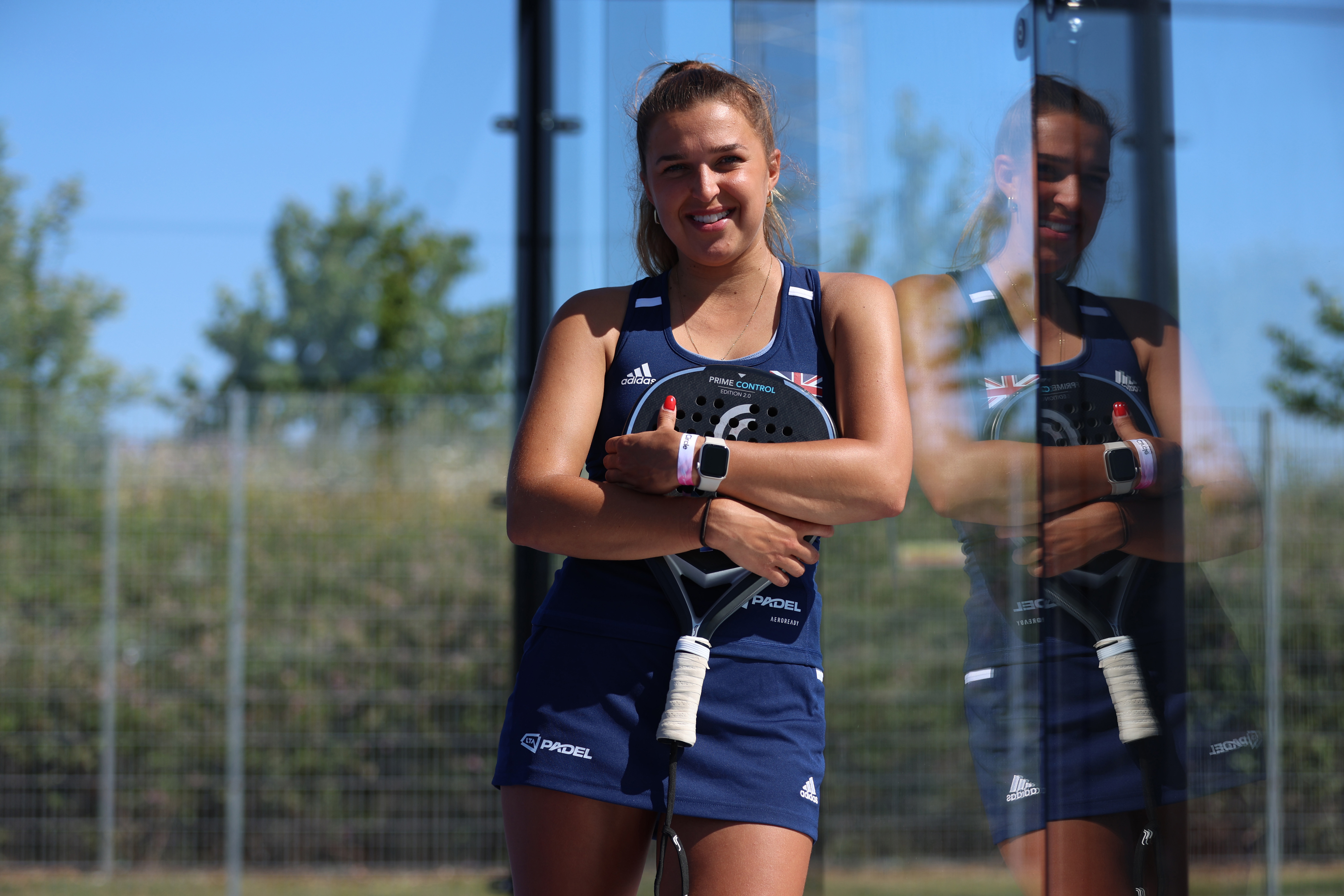 Catherine Rose leaning against the padel court glass with her racket