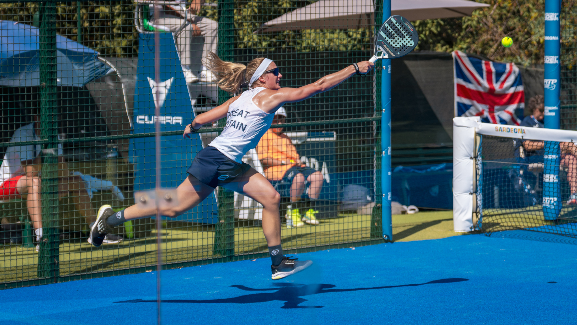 Victoria Nicholas running across the padel court with arm outstretched to reach the ball