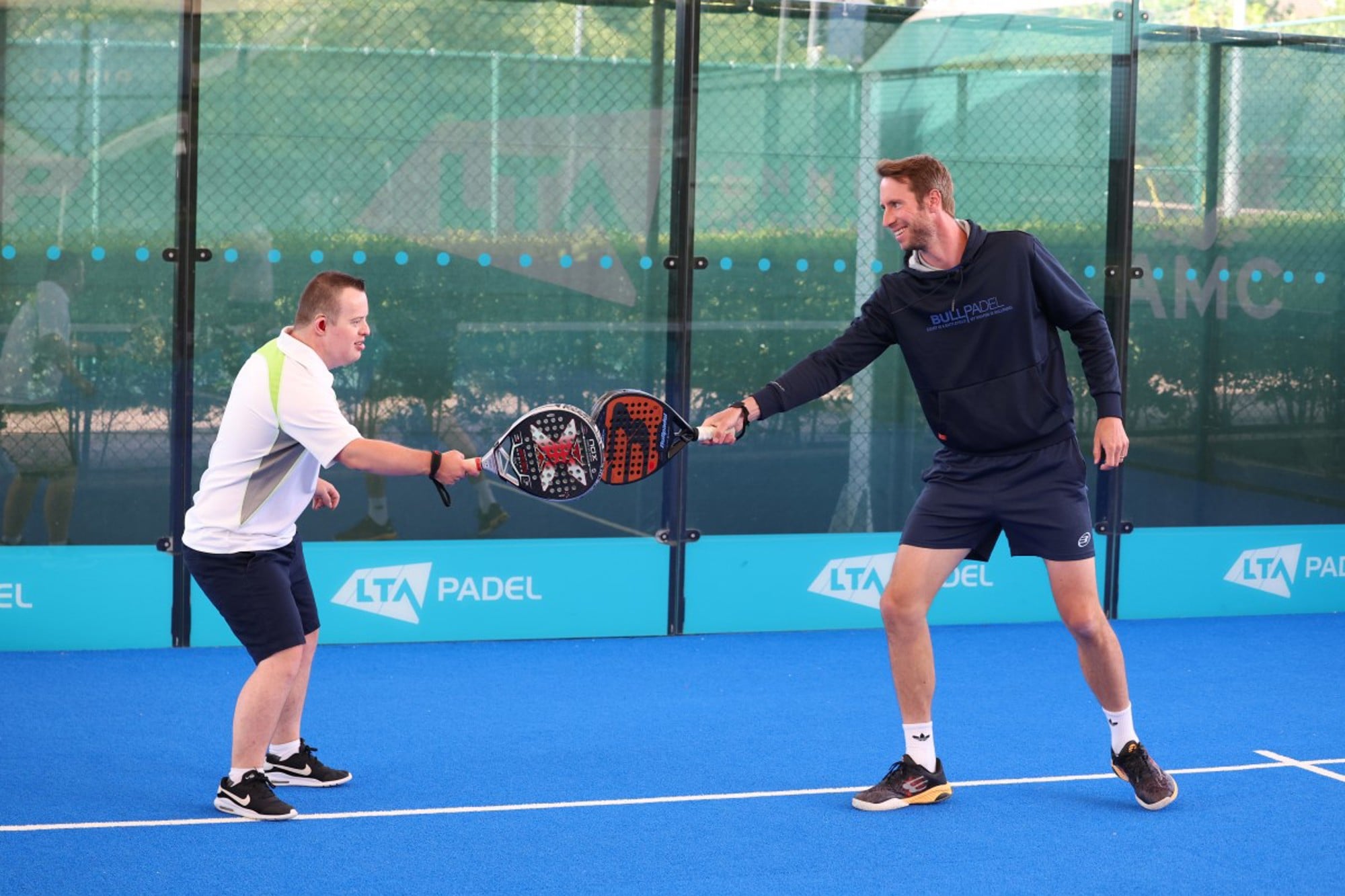 Chris Salisbury and James smiling and hitting padel rackets on the court