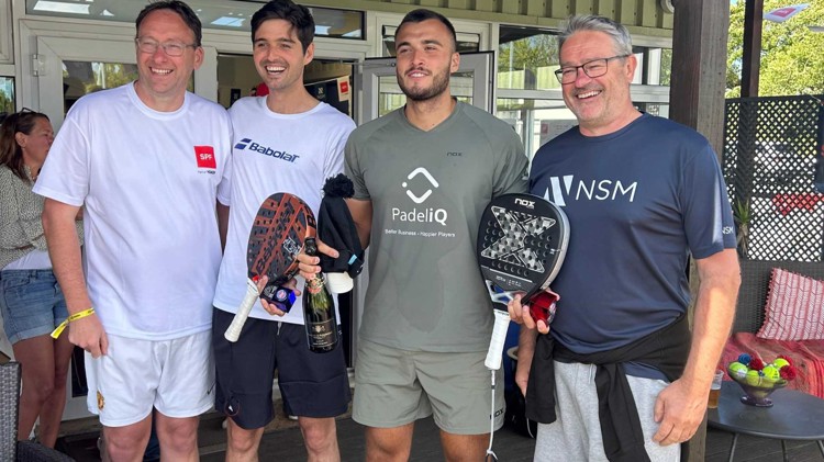 Louie Harris and Rafael Vega holding their padel bats, a bottle of champagne and their trophies alongside two men at the Padel British Tour event in Guernsey
