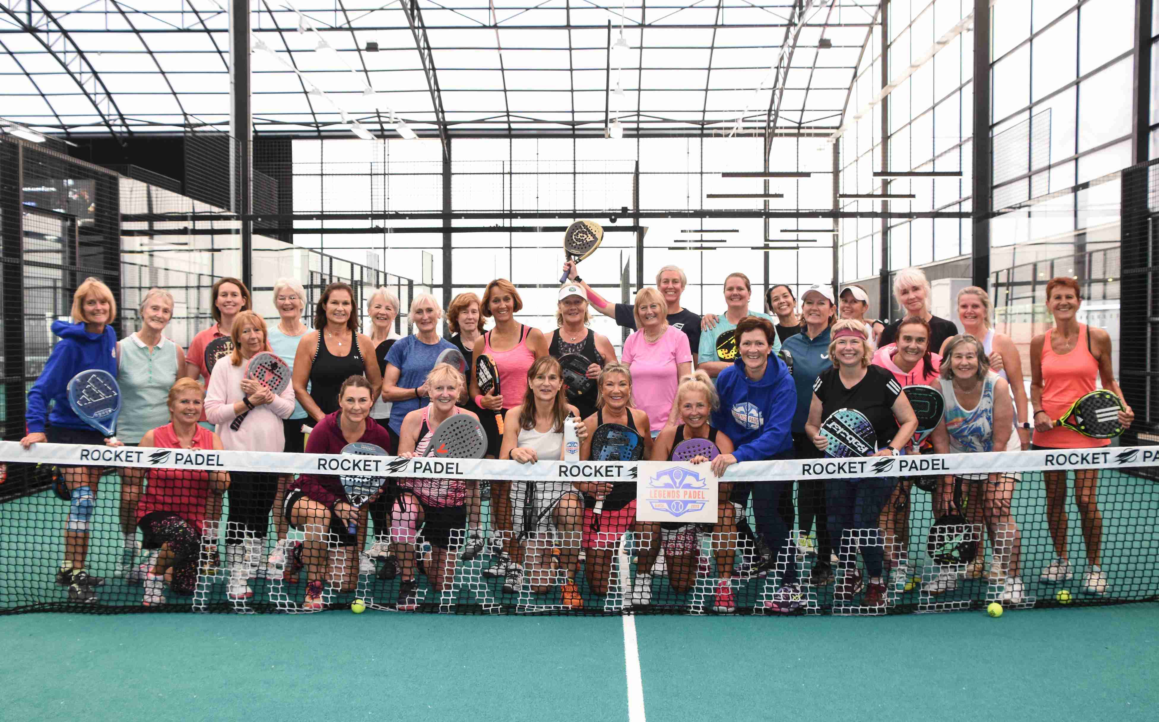 The attendees of the 2024 Female Padel Participation Day posing behind a padel net