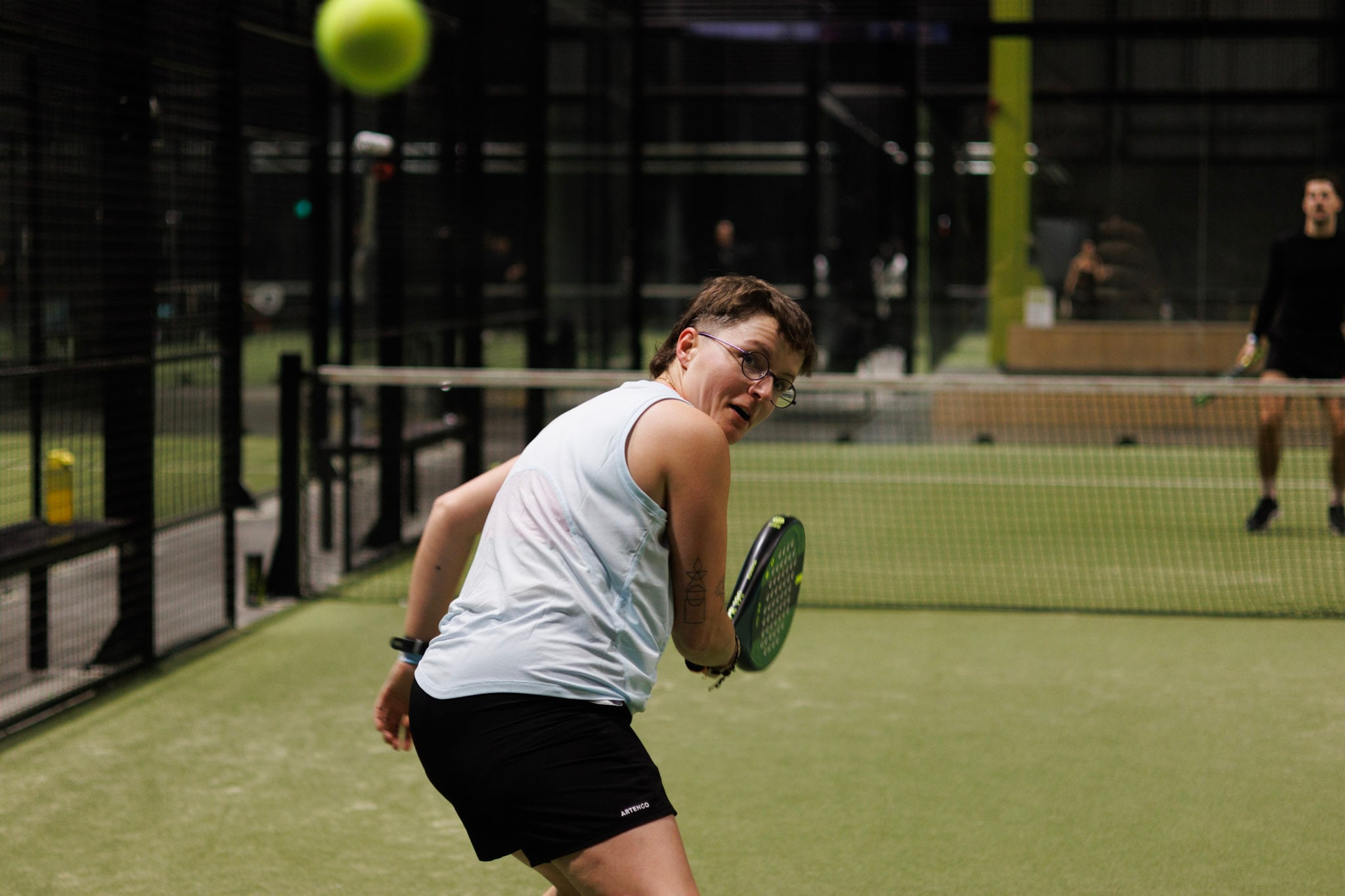 A padel player turning around as a padel ball is about to come towards her 